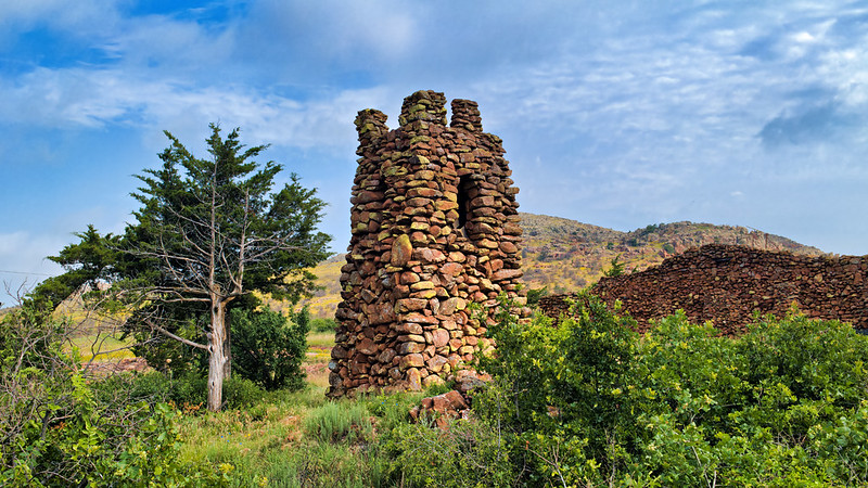 Biblical Tower in the Wichitas Tower built of stacked granite stone blocks with arched window and clouded sky behind.