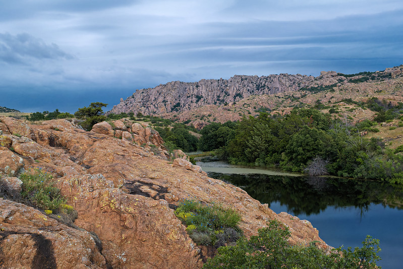 Stormy Skies Over Treasure Lake - Wichita Mountains Wildlife Refuge Rocky granite outcrops and dense green trees surround the still waters of Treasure Lake under a moody, cloud-filled sky at Wichita Mountains Wildlife Refuge.
