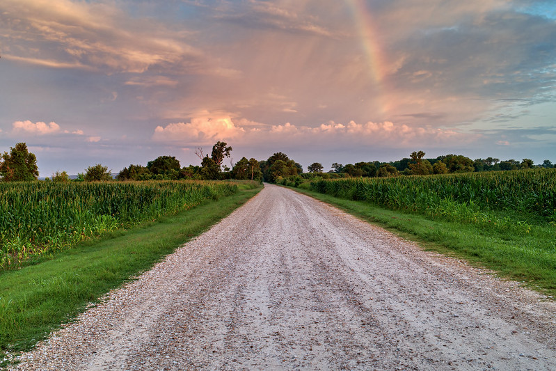 Auto tour gravel road at Sequoyah National Wildlife Refuge in Oklahoma at sunrise with a storm approaching from the west and a rainbow arching over colorful clouds.