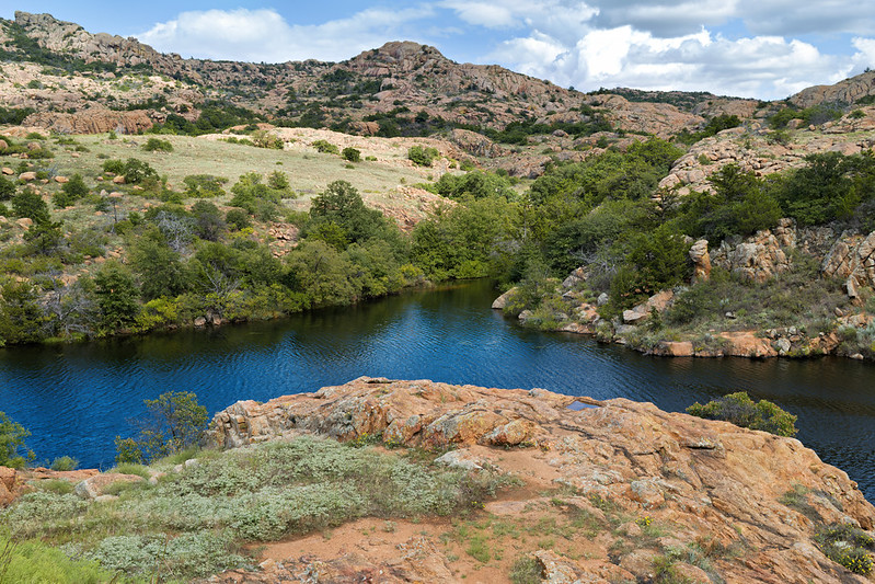 Post Oak Lake with blue water, rocky hills, and scattered trees in the Wichita Mountains Wildlife Refuge.