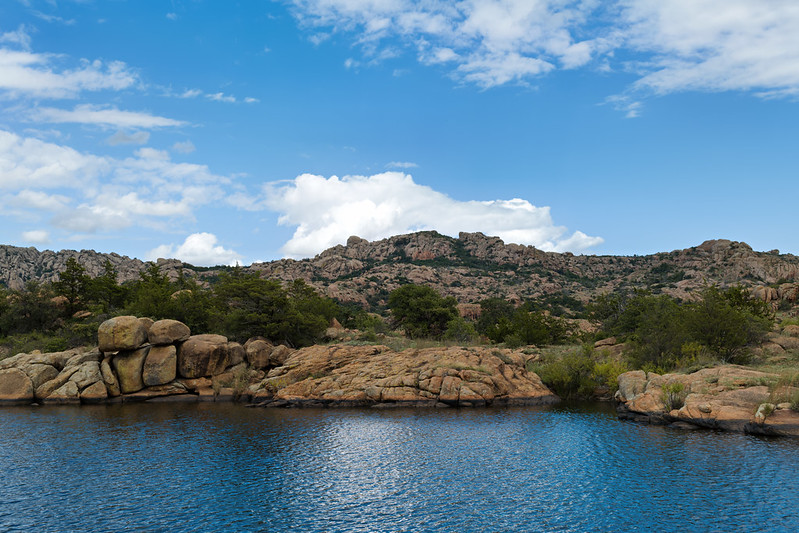 Treasure Lake with rocky shoreline, blue sky, and mountain ridges in the Wichita Mountains Wildlife Refuge.
