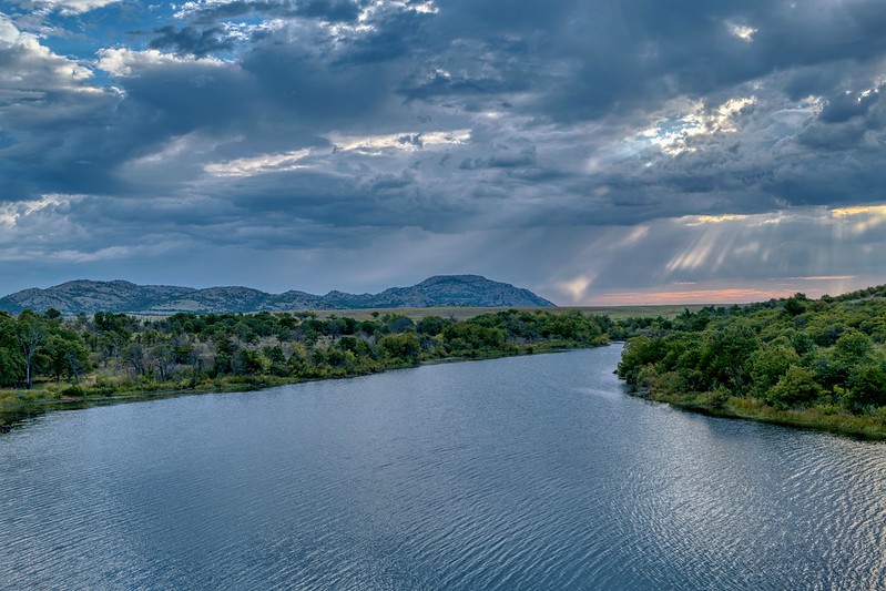 Lake Jed Johnson Oklahoma with sun rays breaking through dark storm clouds over the Wichita Mountains.