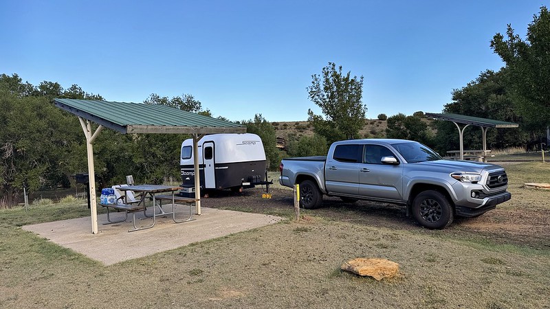 White travel trailer and silver pickup beside a covered picnic table at Black Mesa State Park